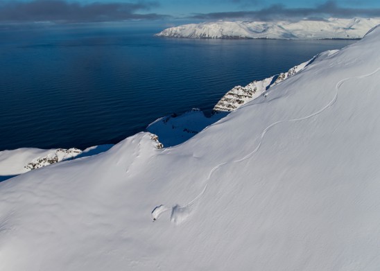 A skier carving down a mountain in powdery snow at ocean's edge.